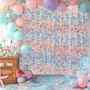 Mermaid-themed birthday party backdrop featuring pastel pink, blue, and gold foil fringe garlands with balloons for a magical celebration.