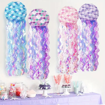 Mermaid jellyfish hanging decorations with iridescent streamers in blue, pink, and purple, displayed above a dessert table.