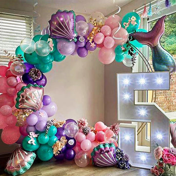 A stunning mermaid-themed balloon arch with pastel purple, teal, and silver balloons, featuring mermaid tail, star, and confetti balloons for a kidsā birthday party decoration.