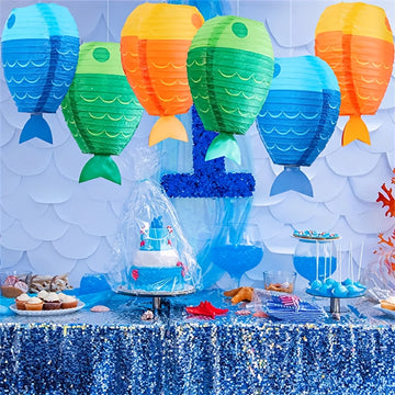 Colorful fish-shaped paper lanterns hanging above a sea-themed birthday party table decorated with a shell and balloons